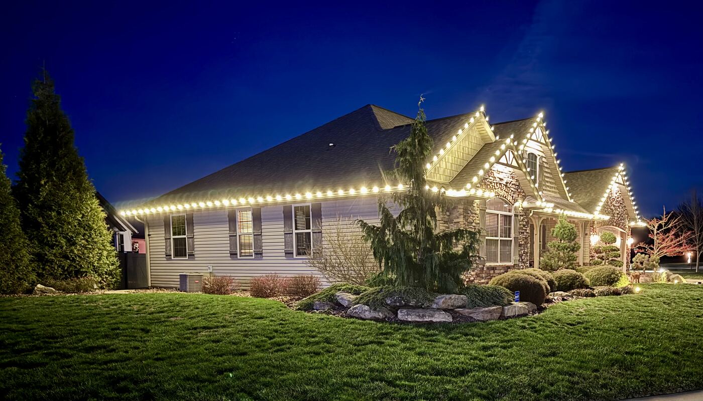 Warm white holiday roofline lighting along a craftsman home's side elevation
